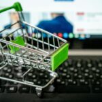 Miniature shopping cart placed on a laptop keyboard, symbolizing online shopping.
