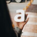 A person holds a 3D letter 'A' on a bustling street, Zapopan, Mexico.
